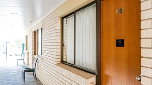 A hotel corridor with a wooden door marked '20', a bench, and a window with curtains. - Capella Hotel Motel (Capella)