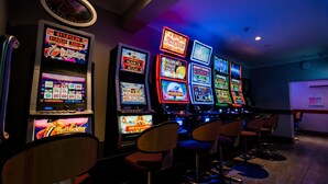 A row of slot machines in a dimly lit room with bar stools. - Capella Hotel Motel (Capella)