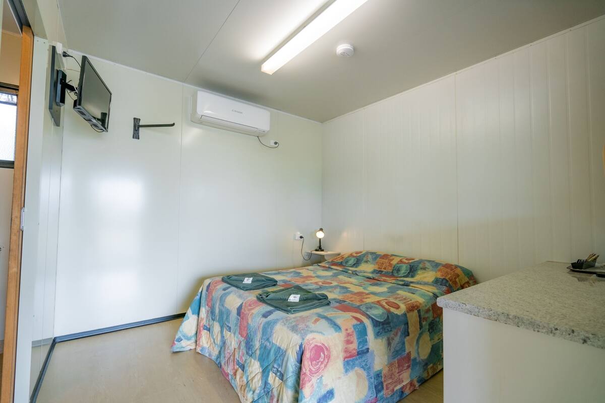 Una habitación pequeña y limpia con cama, escritorio y televisor montado.