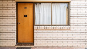 A wooden door with a number plate, a window with curtains, and a brick wall. - Capella Hotel Motel (Capella)