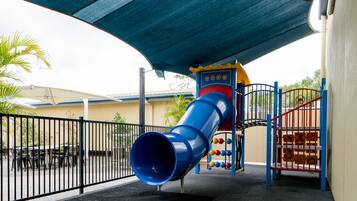A playground with a blue slide, a red and yellow climbing structure, and a black fence.