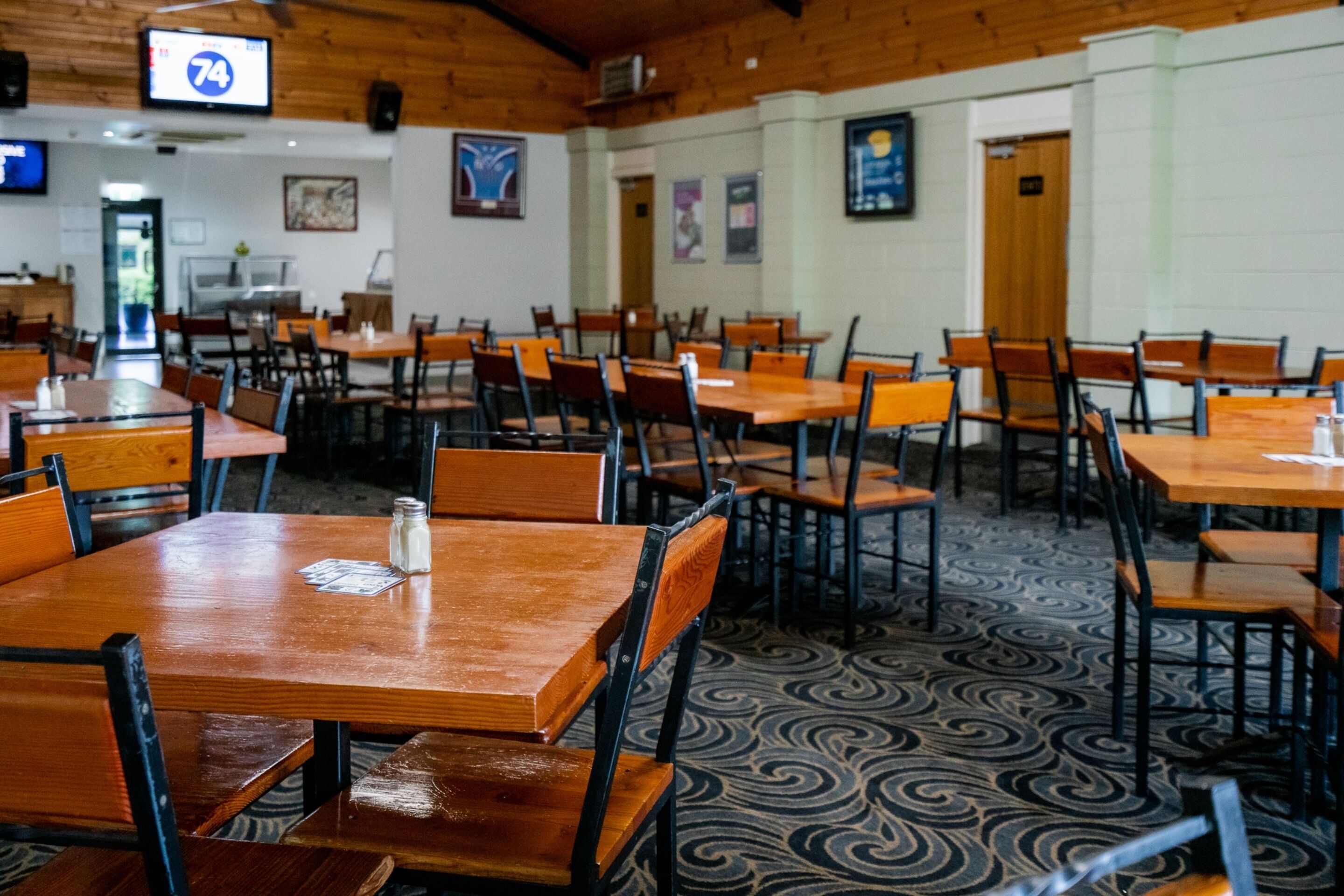 Un restaurant amb taules i cadires de fusta, un terra amb dibuixos i un televisor que mostra el número 74.
