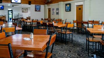 Un restaurant amb taules i cadires de fusta, un terra amb dibuixos i un televisor que mostra el número 74.