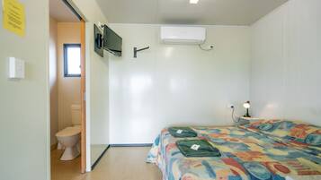 A bedroom with a bed, an air conditioner, a TV mounted on the wall, and a window.