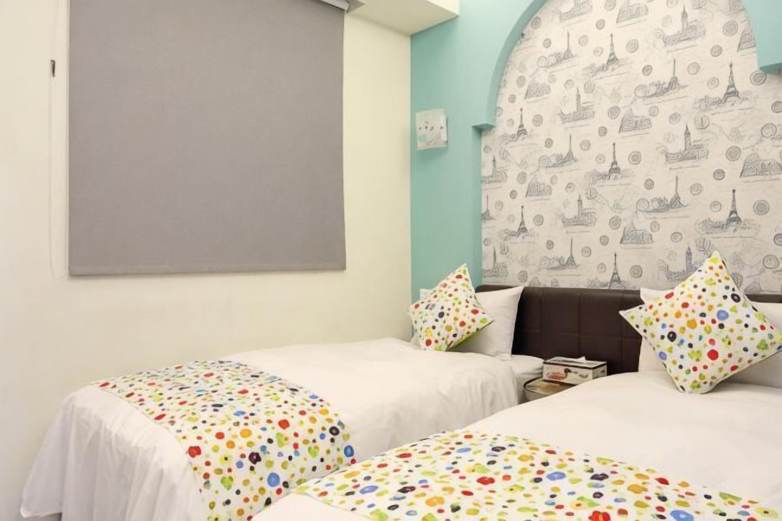 A room with two beds, a large window, a patterned headboard, and a grey wall.