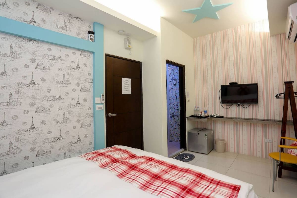 A hotel room with a bed, a television, a desk, and a bathroom.