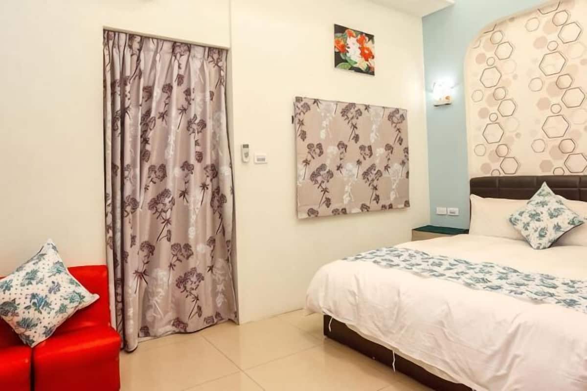 A bedroom with a bed, a red chair, a curtain, and a wall with a floral pattern.