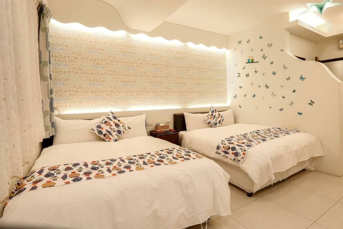 A hotel room with two beds, a nightstand, a wall with butterfly decals, and a ceiling light.