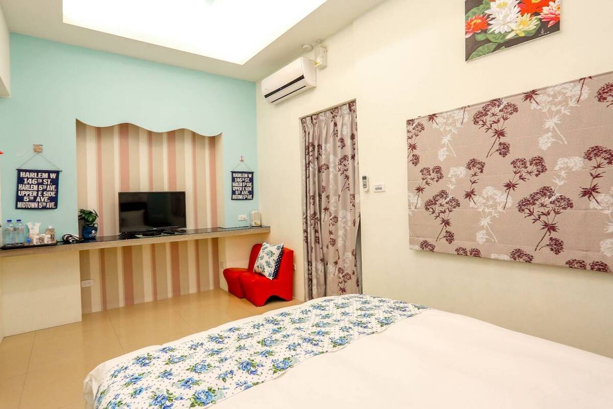 A hotel room with a bed, a TV, a red chair, a floral curtain, and a wall with a floral print.