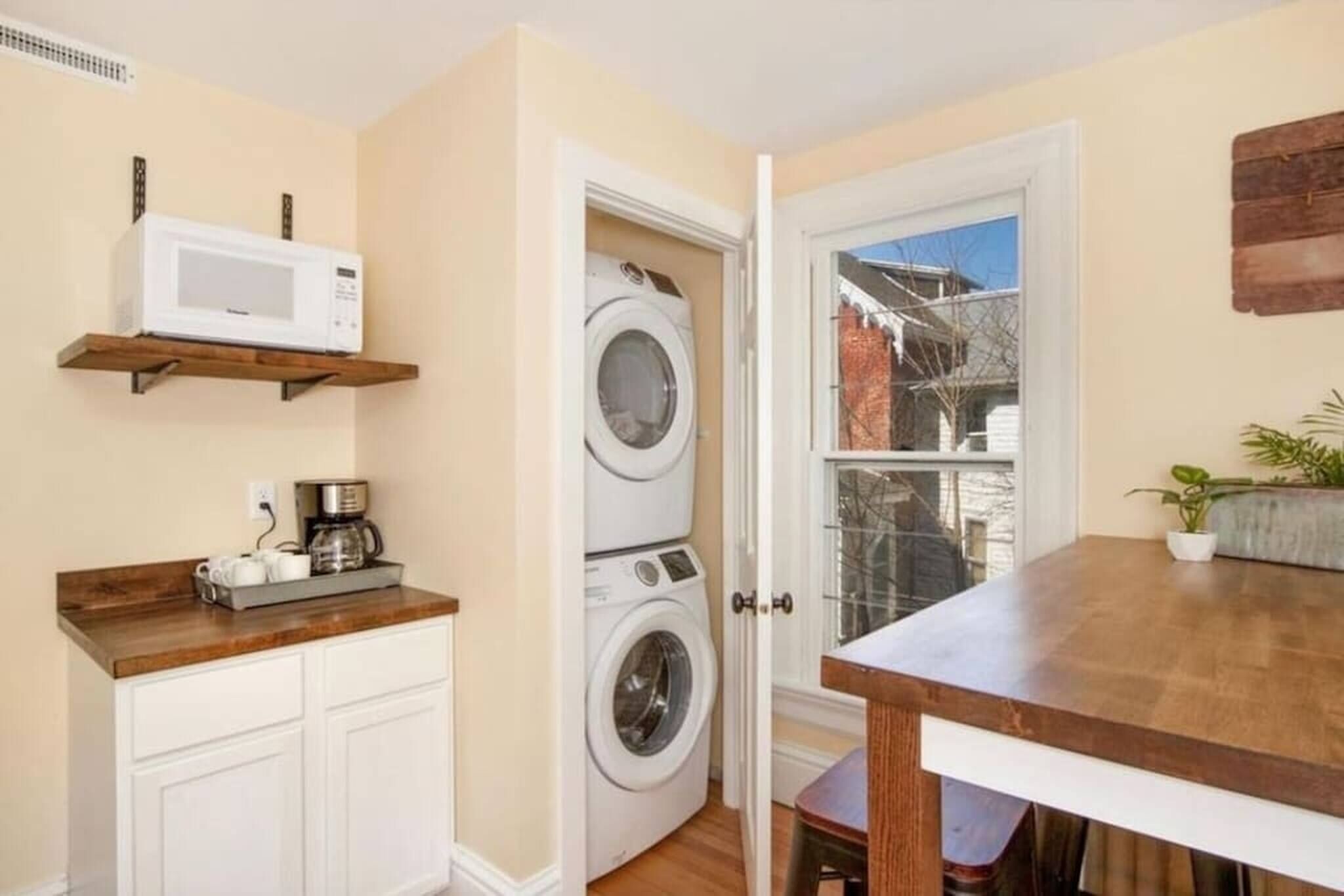A compact laundry room with a washing machine, a microwave on a shelf, and a coffee maker on the counter.