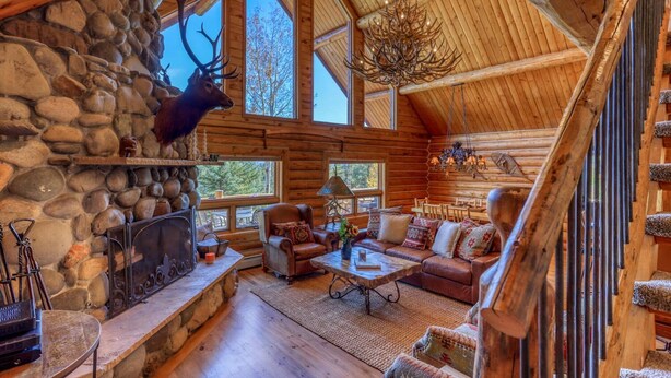 A log cabin interior with a stone fireplace, leather furniture, and a chandelier.