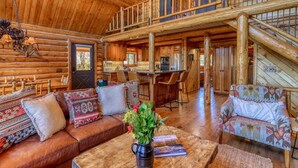 A spacious log cabin interior with a dining area, kitchen, and a large wooden staircase.