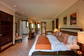 A spacious hotel room with a large bed, a sitting area with a chair, a vanity with a mirror, and a view of the outside. - Eden Confort (Mahé Island)