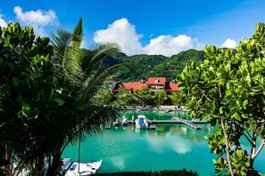 A marina with boats, a red-roofed building, and lush greenery in the background.