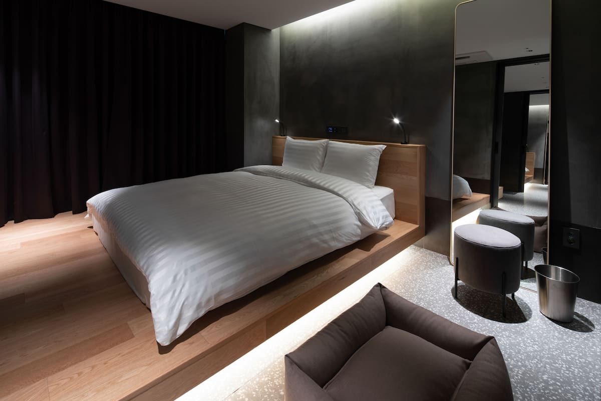 Una habitació d'hotel moderna amb un llit gran, un panell de capçalera de fusta, una petita zona de seients i un mirall.