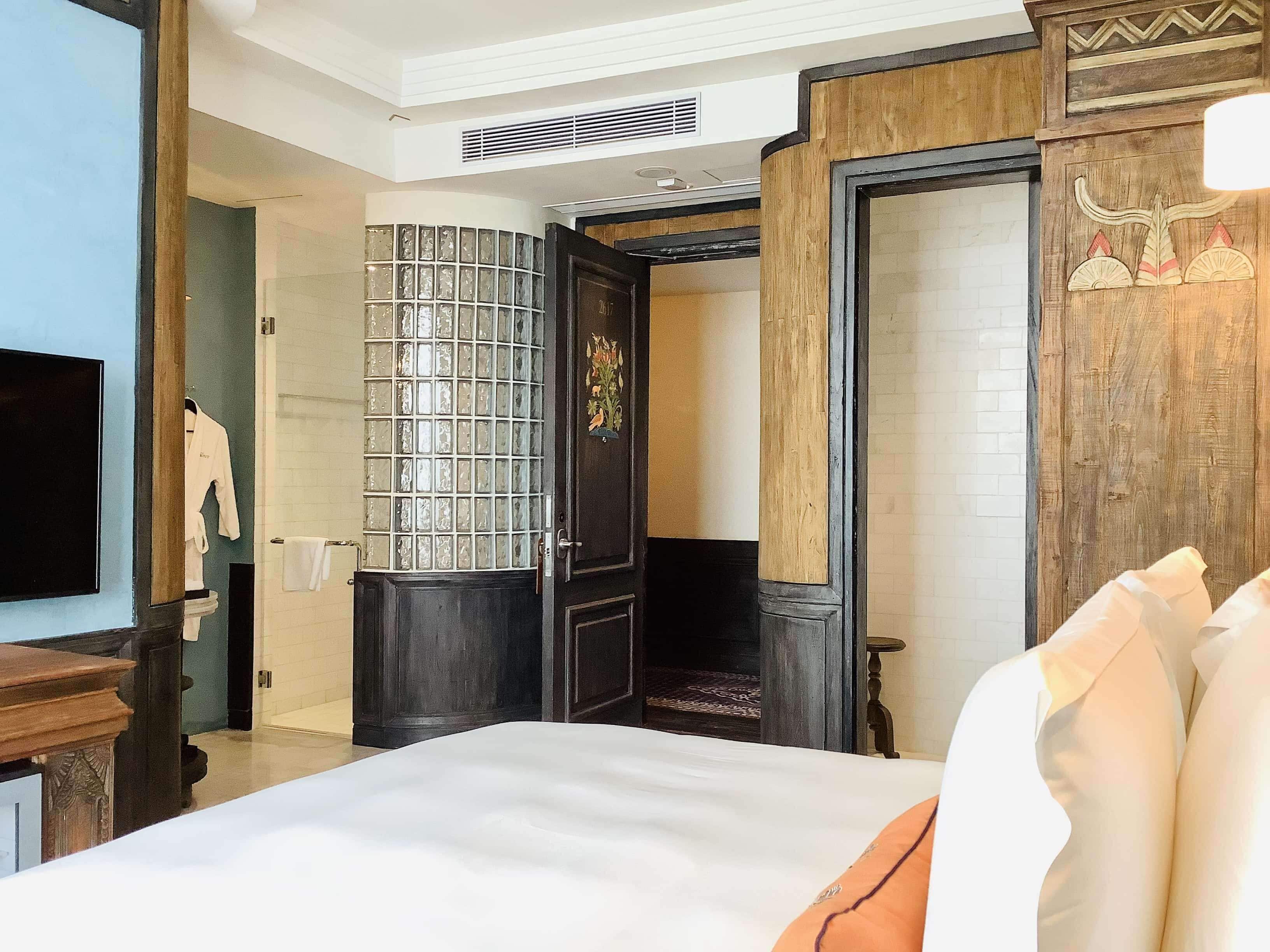 A hotel room with a large bed, a wooden wardrobe, a tiled wall, and a television.