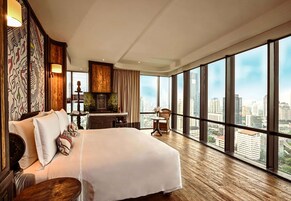 A spacious hotel room with a large bed, a wooden floor, a city view through large windows, and a decorative wall with a patterned design.