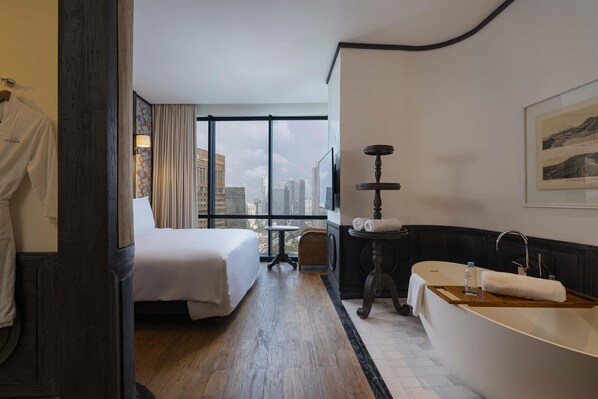 A hotel room with a large bed, a bathtub, a small table, and a view of the city.