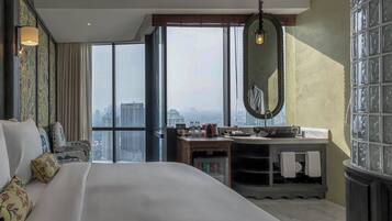 A hotel room with a large bed, a vanity with a mirror, and a view of the city through large windows.