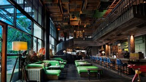 Een ruime binnenruimte met groene zitplaatsen, een bar en grote ramen met uitzicht op groen.