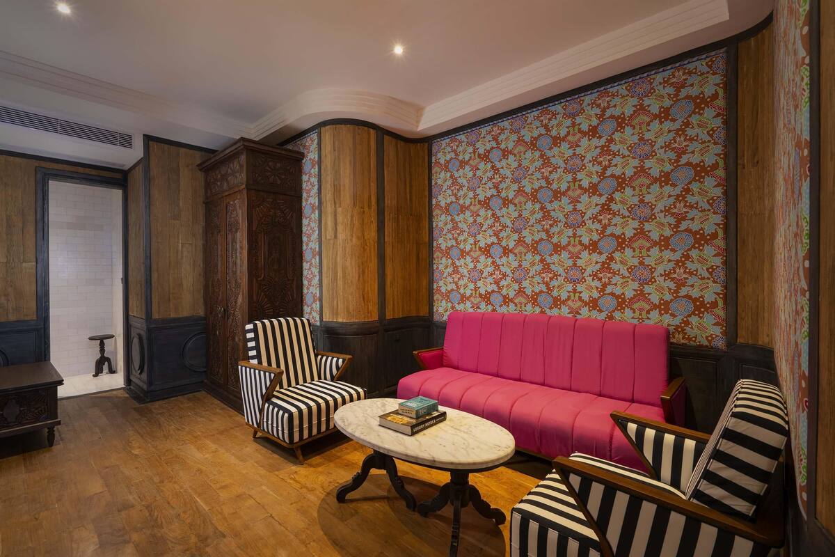 Een kamer met een houten vloer, een rode bank, gestreepte fauteuils en een marmeren tafel met boeken.