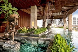 Un área de piscina interior moderna con una escultura singular, una fuente escalonada y abundante vegetación.