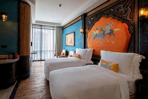 A hotel room with two beds, a wooden accent wall, a framed picture, and a large window with curtains.