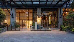 Ein moderner Hotelzugang mit Glasfassade, überdachter Empfangsbereich und einem gepflasterten Weg.