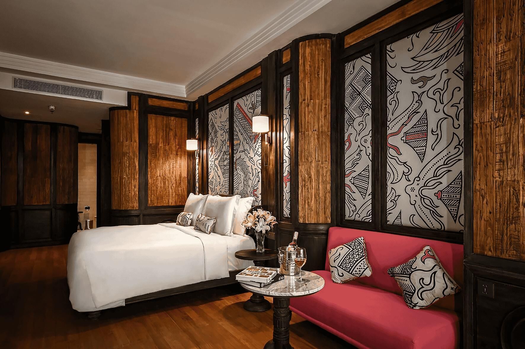 A hotel room with a large bed, a red sofa, and patterned wallpaper.