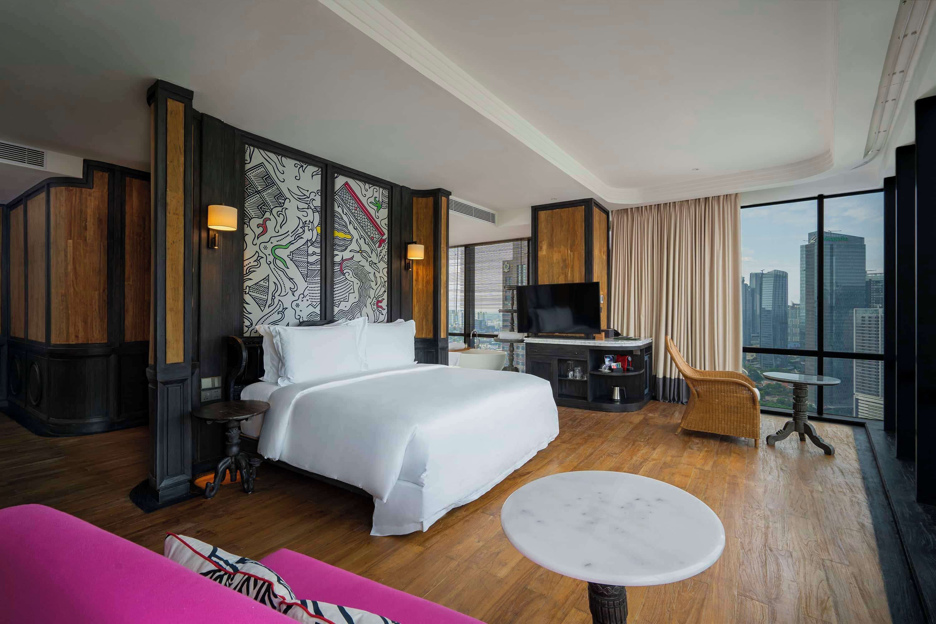 A hotel room with a large bed, a TV, a desk, and a view of the city.