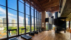 Een ruime fitnessruimte met grote ramen en uitzicht over de stad, houten vloeren en fitnessapparatuur.