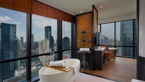Een moderne badkamer met een vrijstaand bad, een houten wastafelmeubel en een groot raam met uitzicht op de stad.