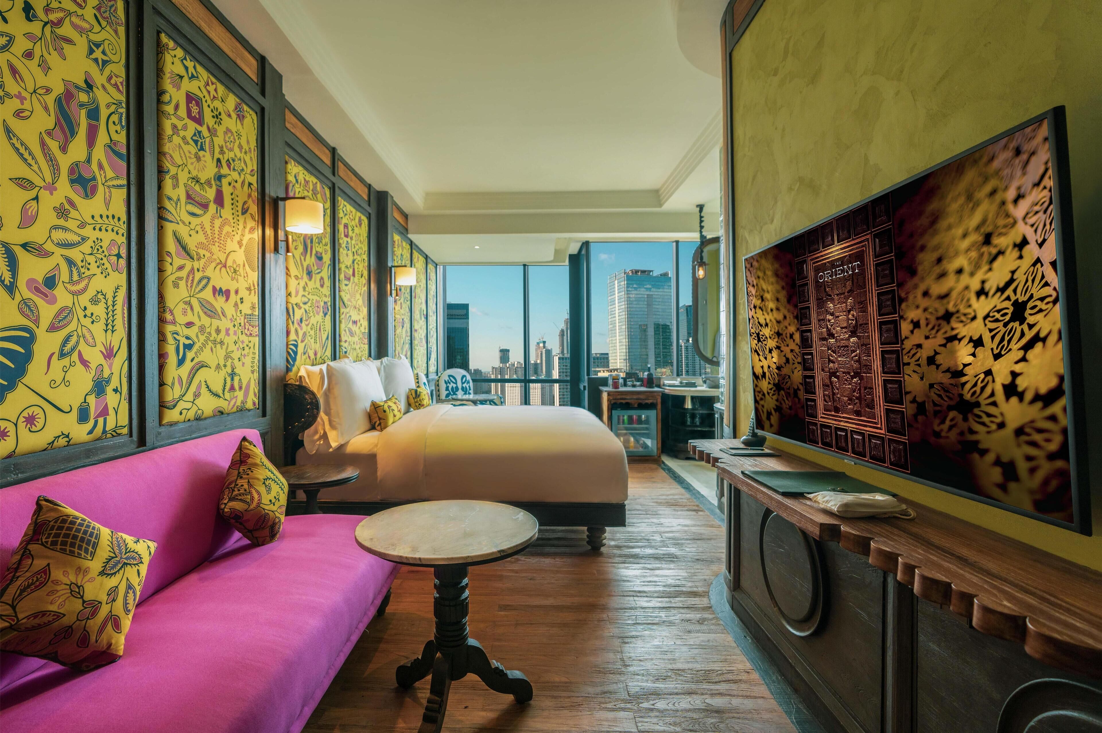 Habitación de hotel con cama, sofá rosa, una mesita redonda y vistas a la ciudad.