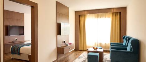 A modern hotel room with a bed, a TV, a desk with a chair, and a sofa.