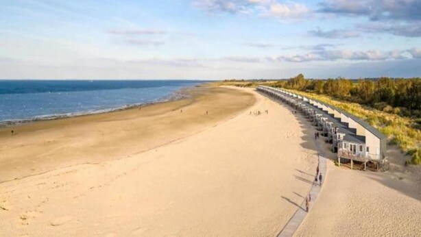 Une plage bordée d’une longue rangée de cabanes de plage.
