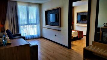 Habitación de hotel con piso de madera, un escritorio con silla, un televisor montado en la pared y una cama con manta roja.