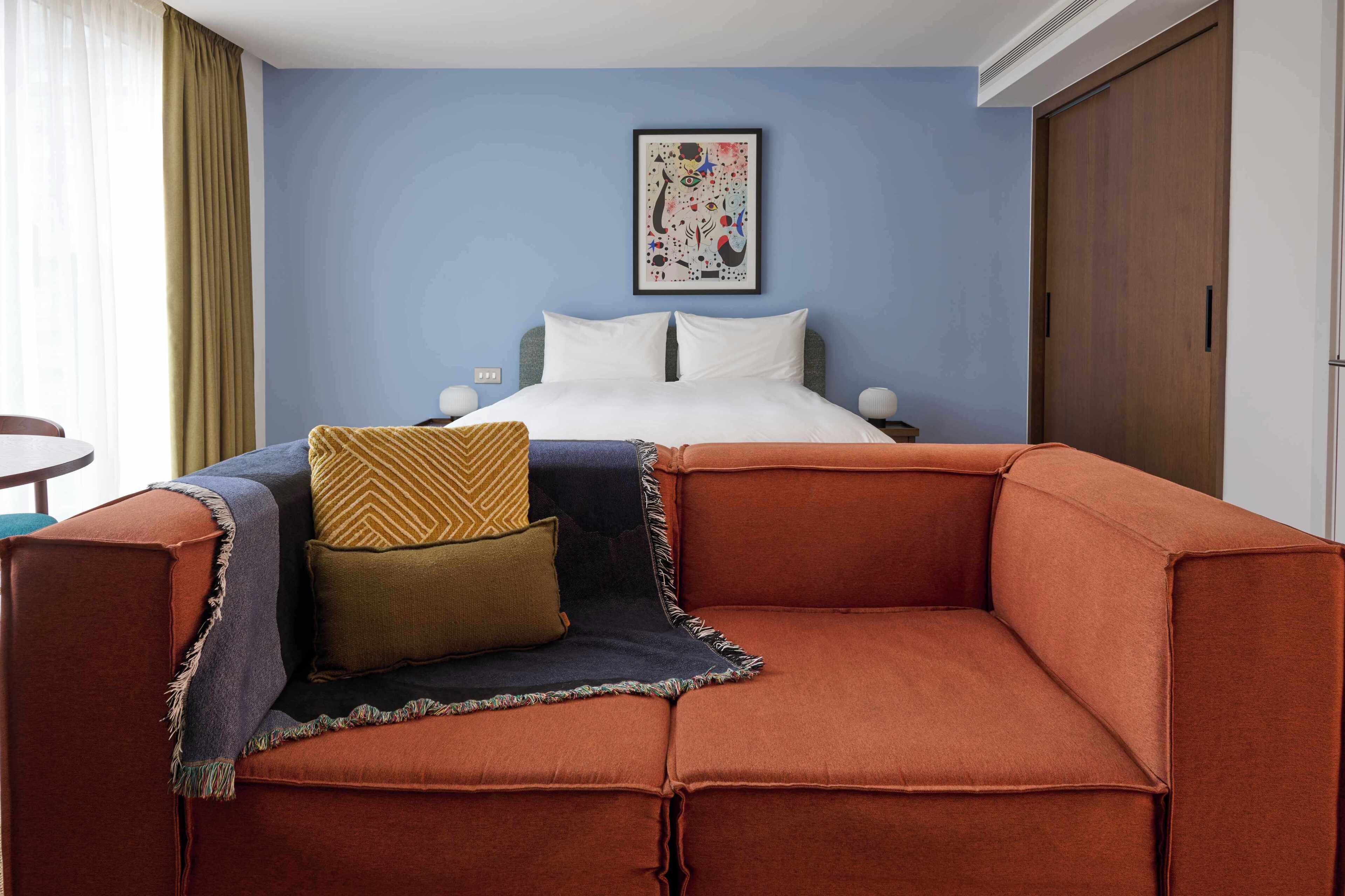 Habitación de hotel con cama, sofá, una obra de arte enmarcada en la pared y ventana con cortinas.
