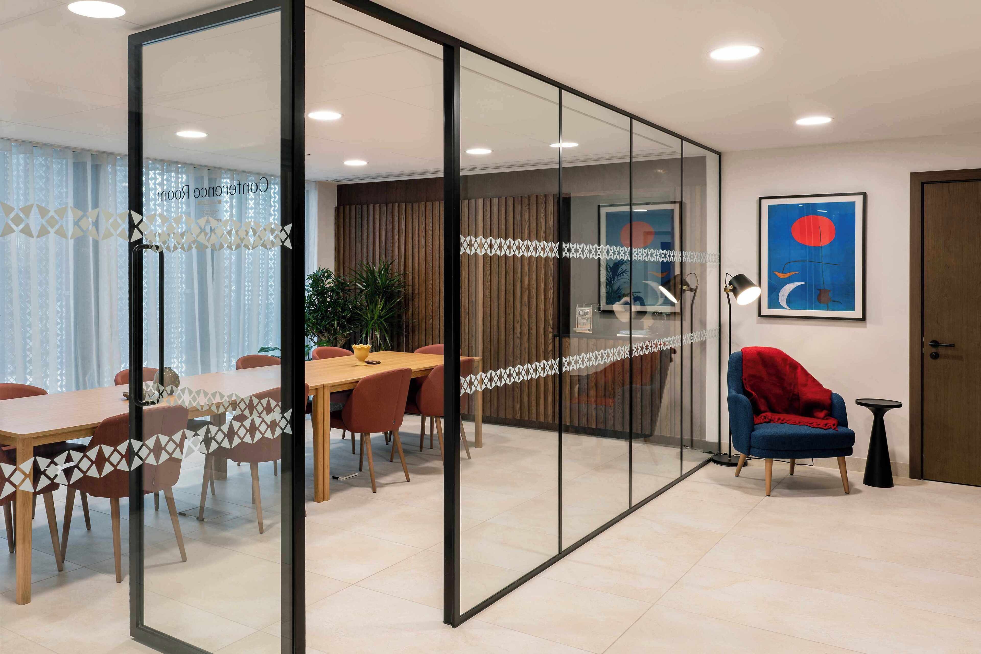 A modern meeting room with glass partitions, wooden tables, and red chairs.