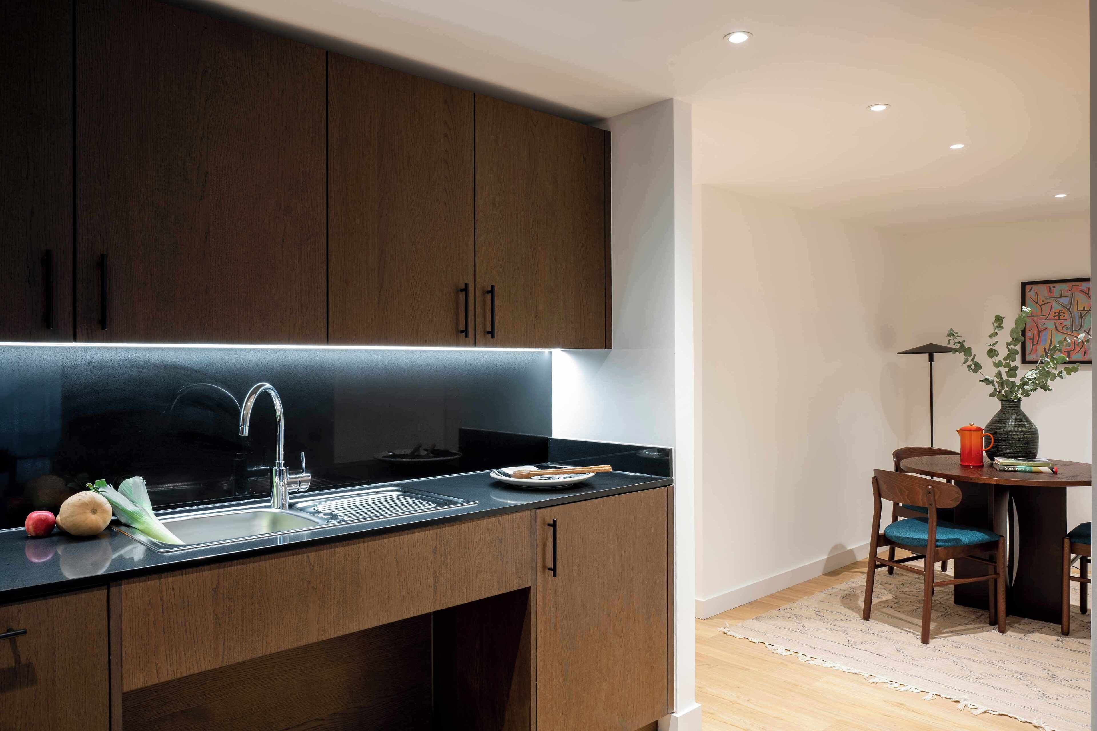 A modern kitchen with dark wooden cabinets, a stainless steel sink, and a dining area with a table and chairs.