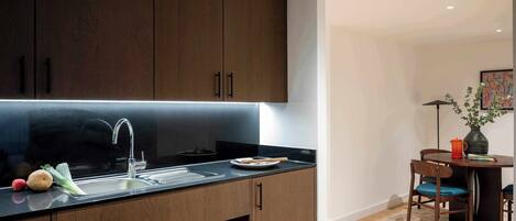 A modern kitchen with dark wooden cabinets, a stainless steel sink, and a dining area with a table and chairs.
