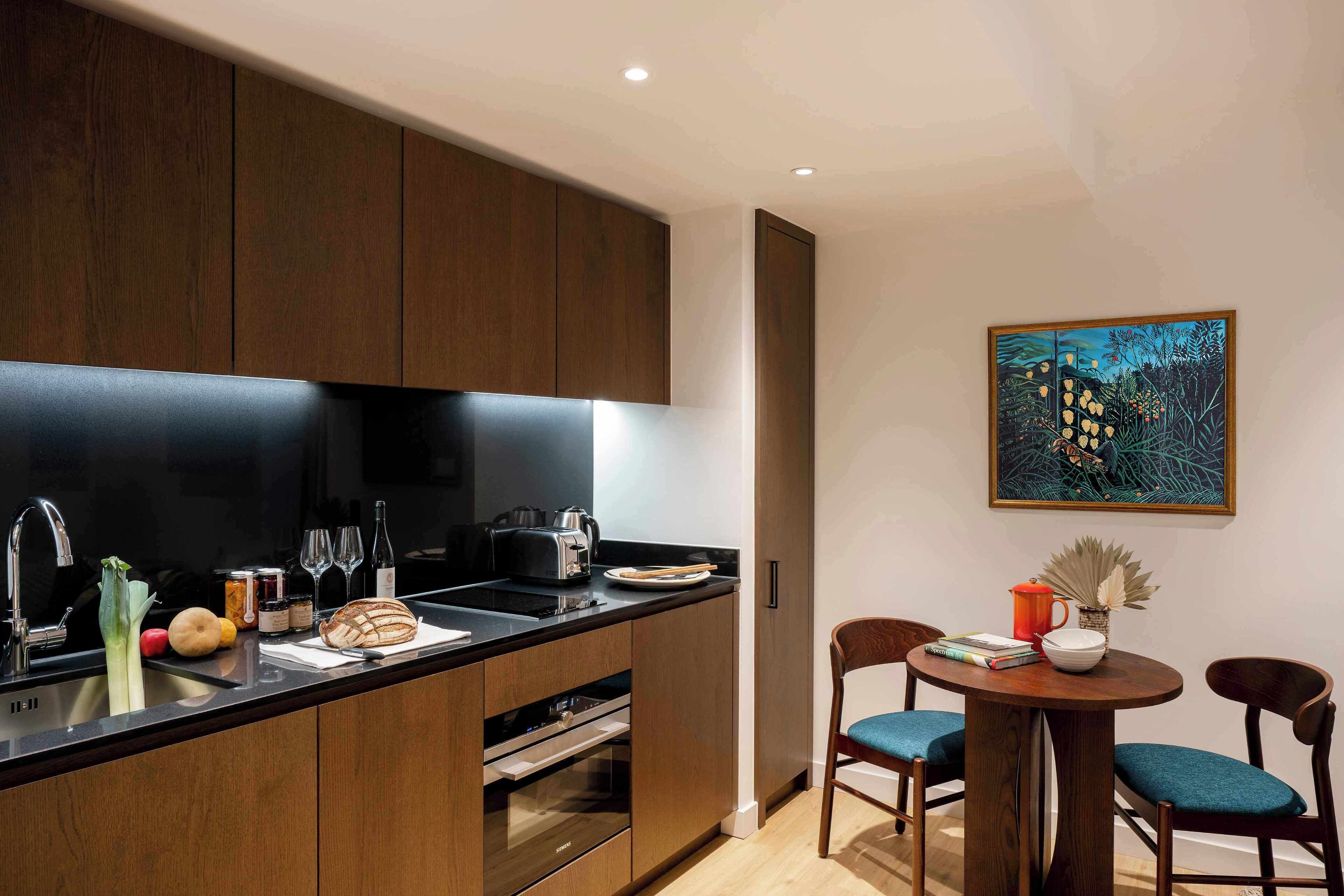 A modern kitchen with dark wooden cabinets, a black countertop, and a dining area with two chairs and a table.