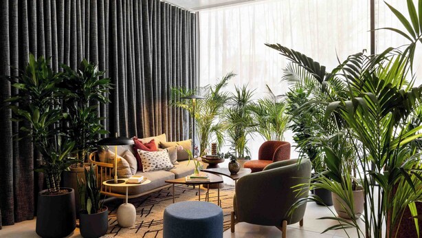 A modern living room with a sofa, armchairs, and a coffee table. There are multiple potted plants and a large window with curtains. - Cove Landmark Pinnacle (London)