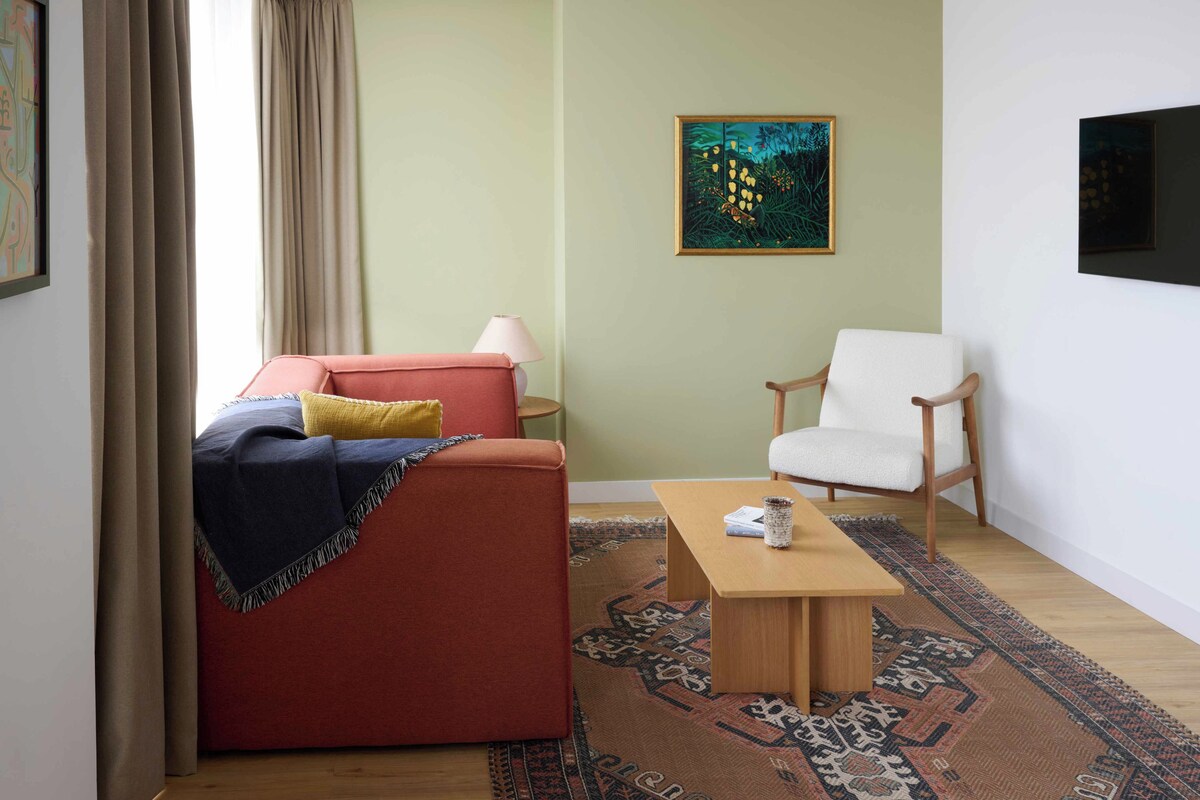 A living room with a red sofa, a white armchair, a wooden coffee table, and a patterned rug.