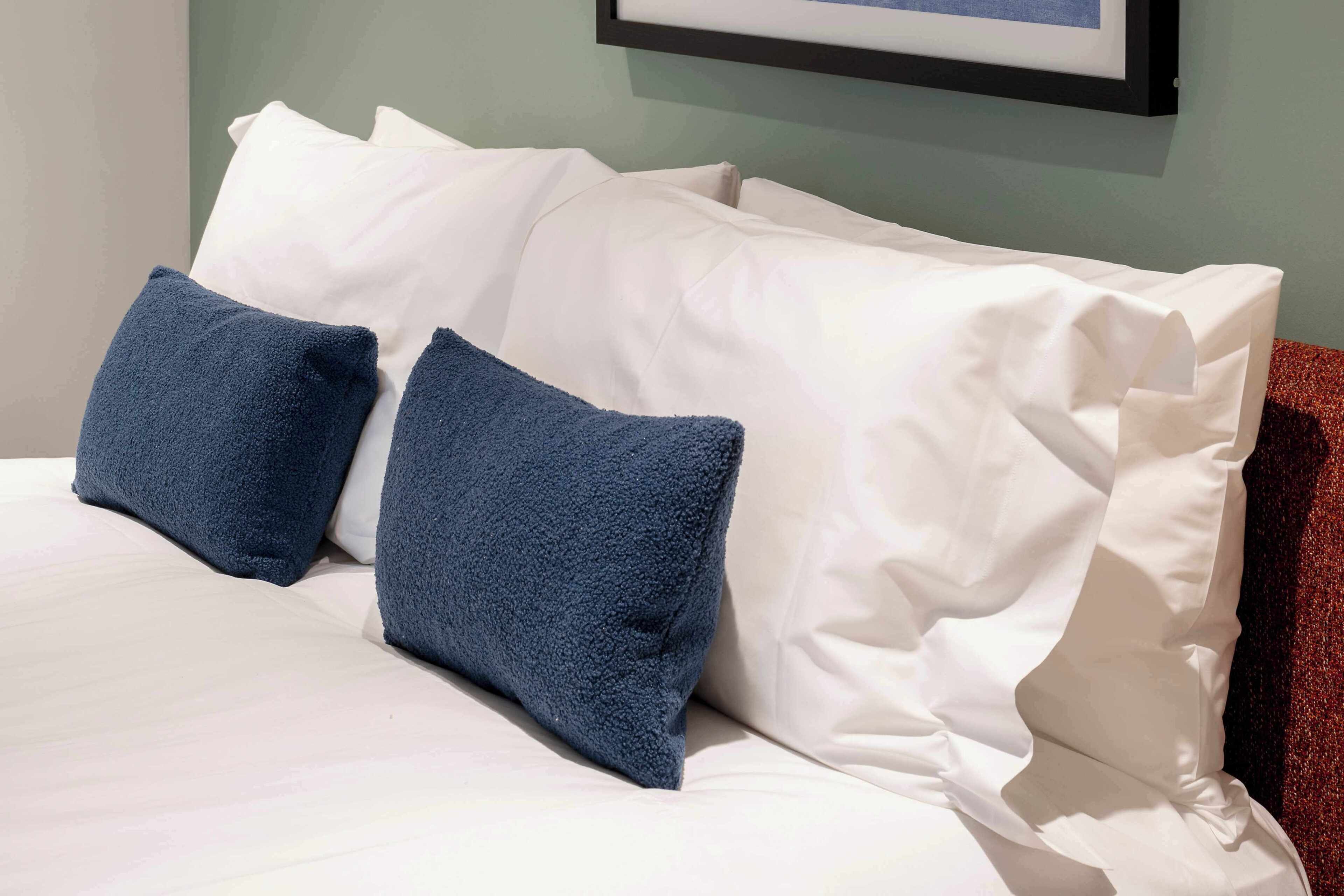 A bed with white linens and two blue pillows.