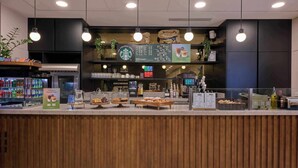 A Starbucks coffee shop counter with a wooden panel design, a menu board, and various coffee-making equipment. - Cove Landmark Pinnacle (London)