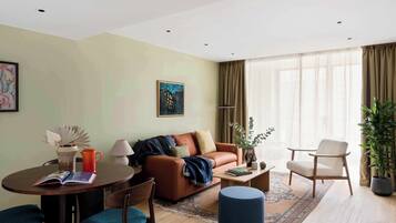 A modern living room with a brown leather sofa, a round coffee table, and a blue ottoman. There is a dining table with chairs and a lamp.