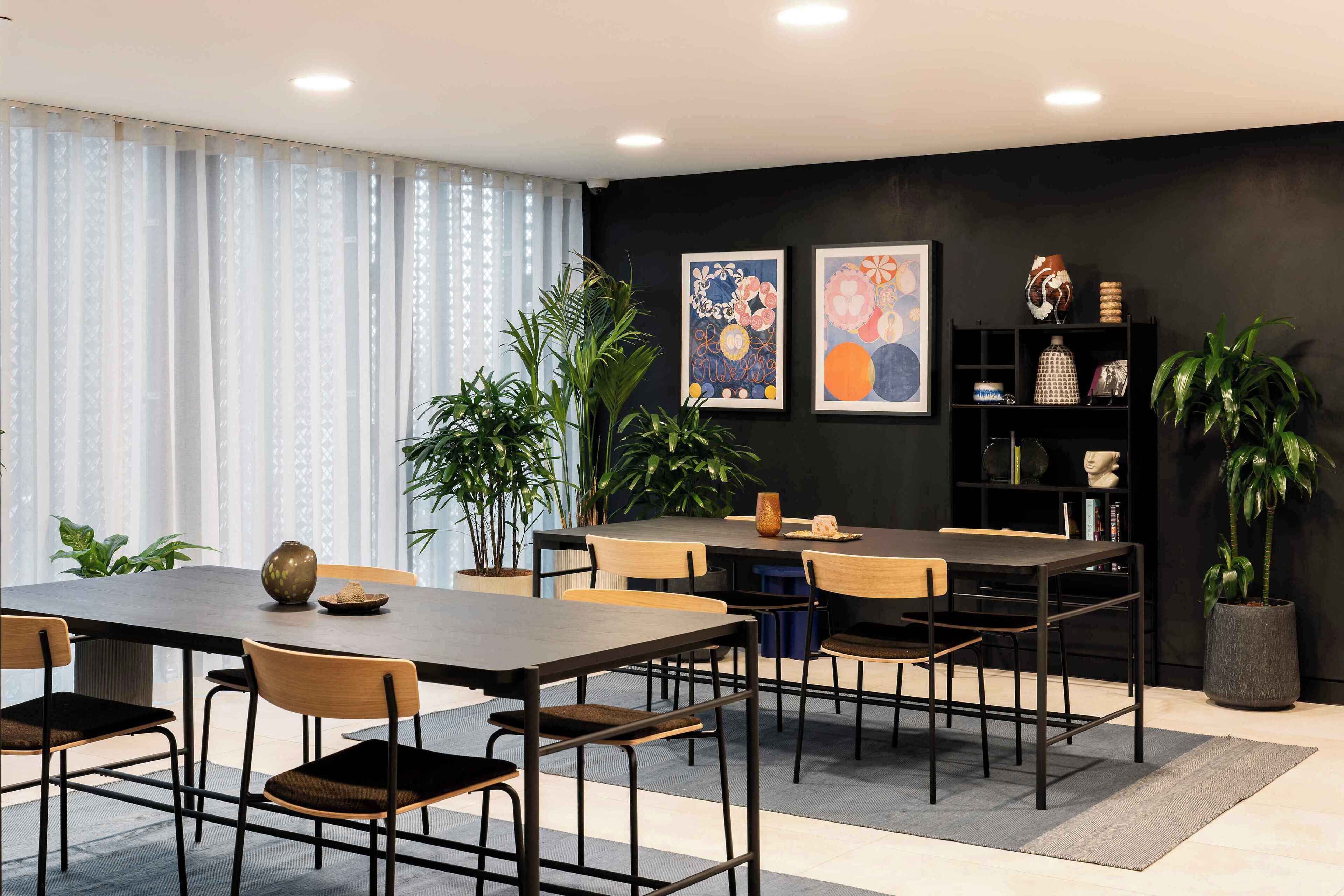 A modern dining area with a dark wooden table and chairs, surrounded by potted plants and artwork on the walls.