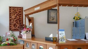 Ein Empfangsbereich mit Holzausstattung, einem gerahmten Kunstwerk an der Wand, einem blauen Aktenschrank und einer Blumenkomposition auf der Theke.
