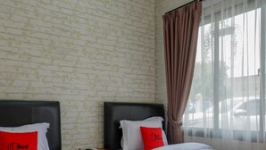 Ein Hotelzimmer mit zwei Betten, jeweils mit roter Bettdecke und Kissen, einem hölzernen Nachttisch und einer Wand mit Ziegeloptik.