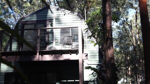 Een chalet van twee verdiepingen met een balkon, omringd door bomen.